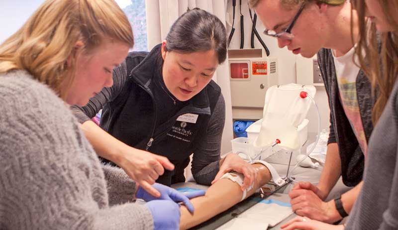 Bomin Shim instructing three undergraduate nursing students