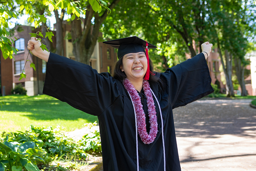 Student celebrating with arms up, graduation gown on