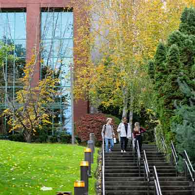 Two students coming down a long stairway on campus with Ames Library in the background.