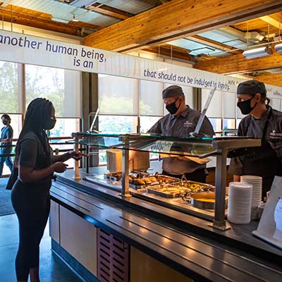 An SPU student choosing food in Gwinn Commons, while two servers prepare what she's like.