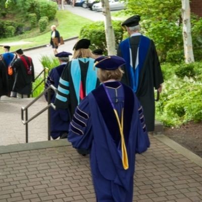 SPU faculty members seen from behind as they walk down a staircase near Martin Square while wearing their regalia.