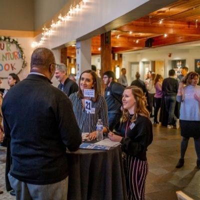 Two female students and a businessman stand at a table at a small café table at a networking event.