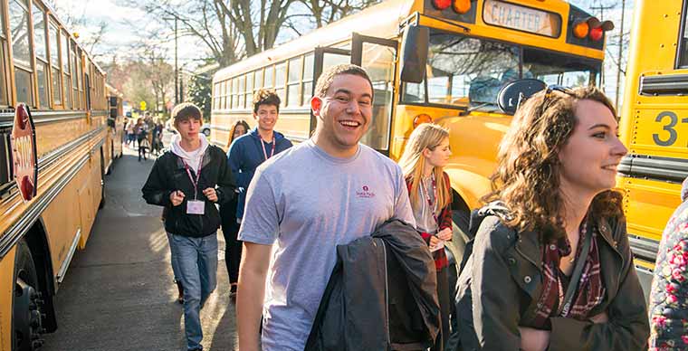 Students shown walking and smiling in front of yellow school buses