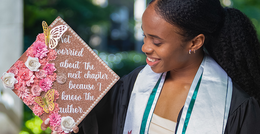 A student holds her morter board which reads "Not worried about the next chapter because I know the author"