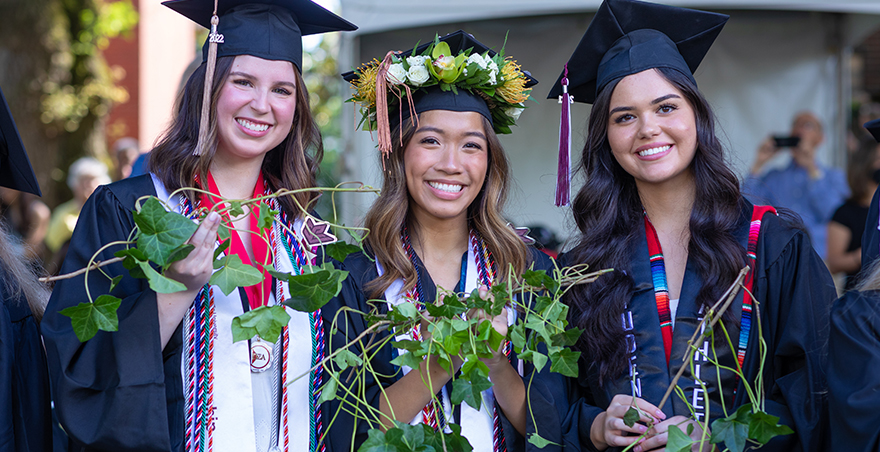 Three female students in their caps and gowns proudly hold their ivy at SPU's Ivy Cutting ceremony