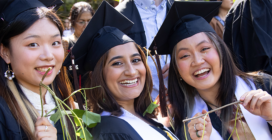 Three female students in their caps and gowns proudly hold their ivy from SPU