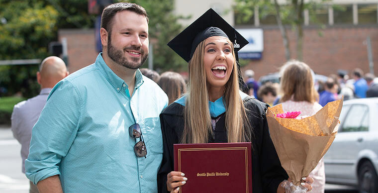 An SPU graduate student holds flowers and poses for the camera at the 2019 Graduate Commencement ceremony - photo by Dan Sheehan