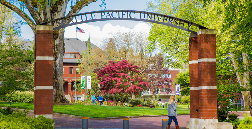 An SPU student walks by the Seattle Pacific University entry archway on a bright spring day